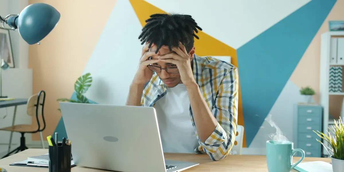 Man holding head in frustration at desk with laptop, the reality of searching for a third-party maintainer